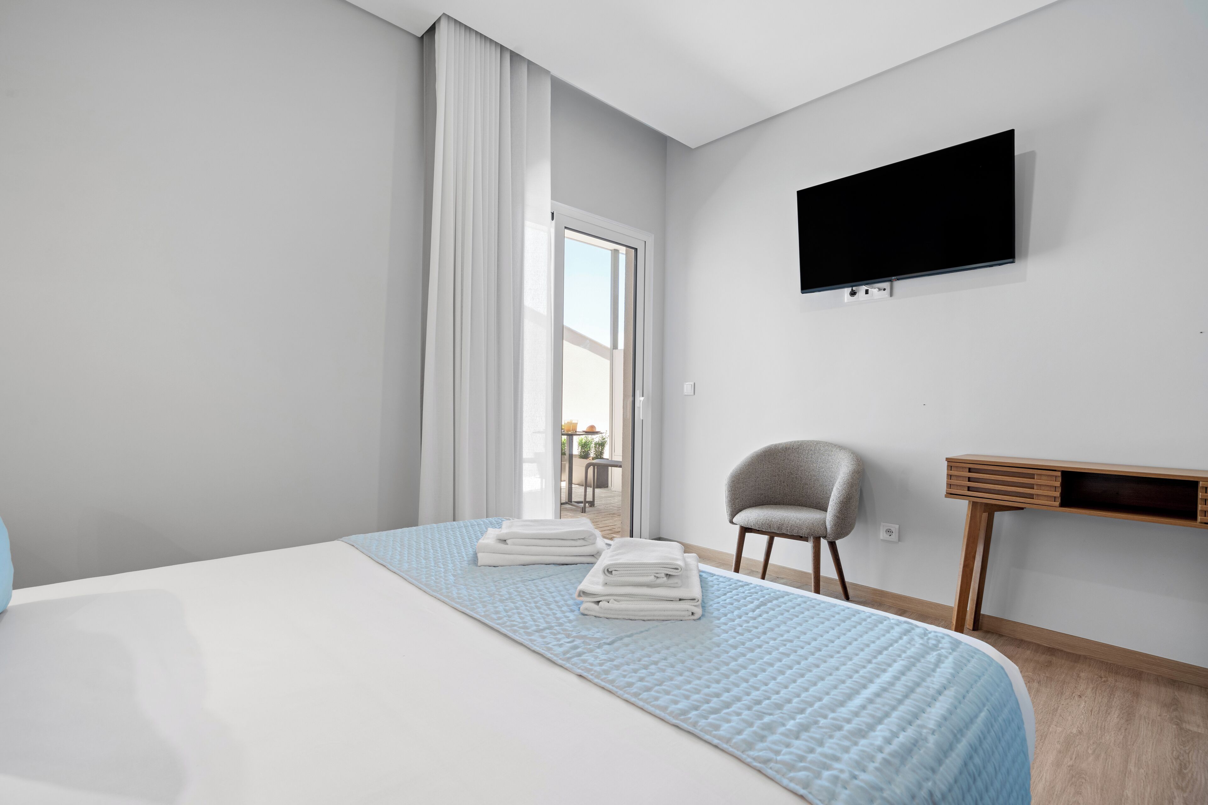 A modern hotel room with a large bed, a desk, and a TV on the wall.
