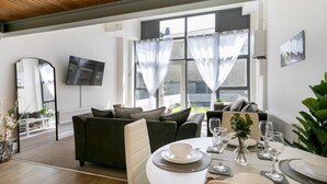 A modern living room with a sofa, dining table set for two, and a large window with sheer curtains. - City Stay • 3 Ensuites • SunTerrace • Free Parking | Pass the Keys (Nottingham)