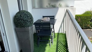 A balcony with artificial grass, a table with chairs, a potted plant, and a view of the street. - Charming apartment in La Baule, close to shops and beach. (La Baule-Escoublac)