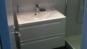 A bathroom with a white sink, a mirror, and a shower. - Charming apartment in La Baule, close to shops and beach. (La Baule-Escoublac)