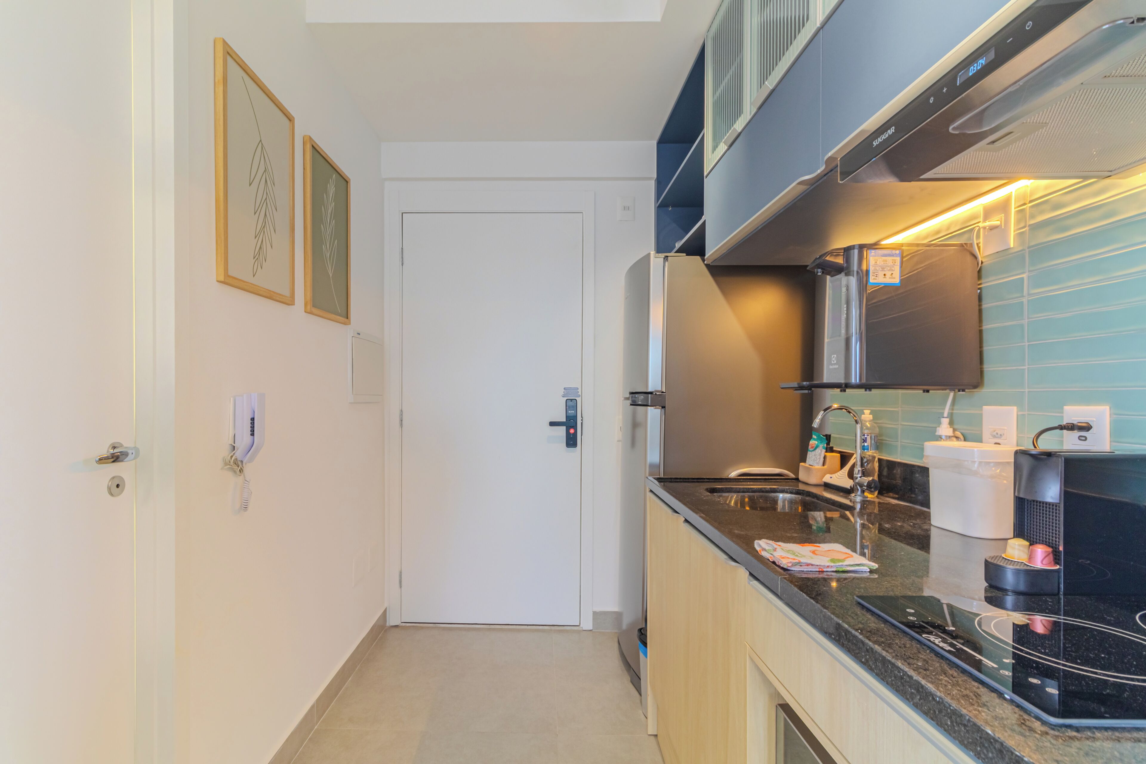 Eine moderne Küche mit Einbauofen, Spüle und Kühlschrank. An der Wand befinden sich gerahmte Bilder und eine Tür mit einem Zahlenschloss.