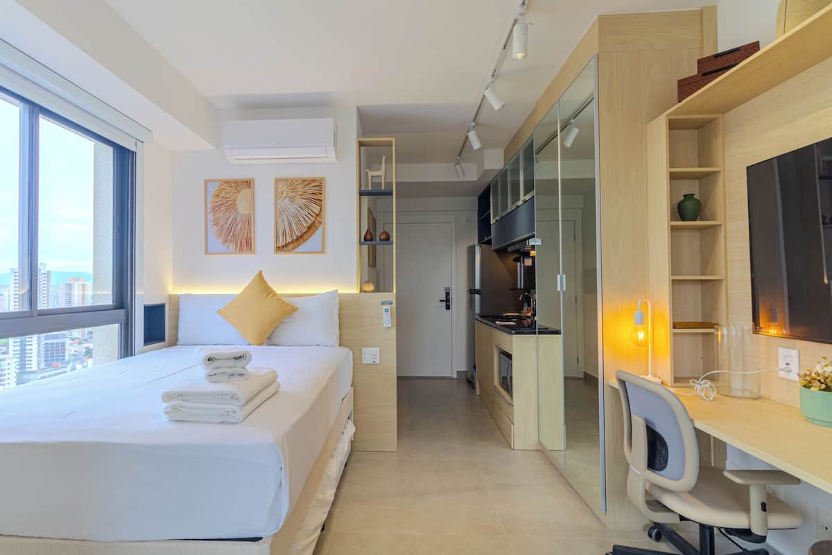 A modern hotel room with a large bed, a desk, and a kitchenette.
