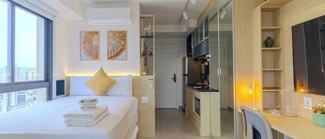 A modern hotel room with a large bed, a desk, and a kitchenette.