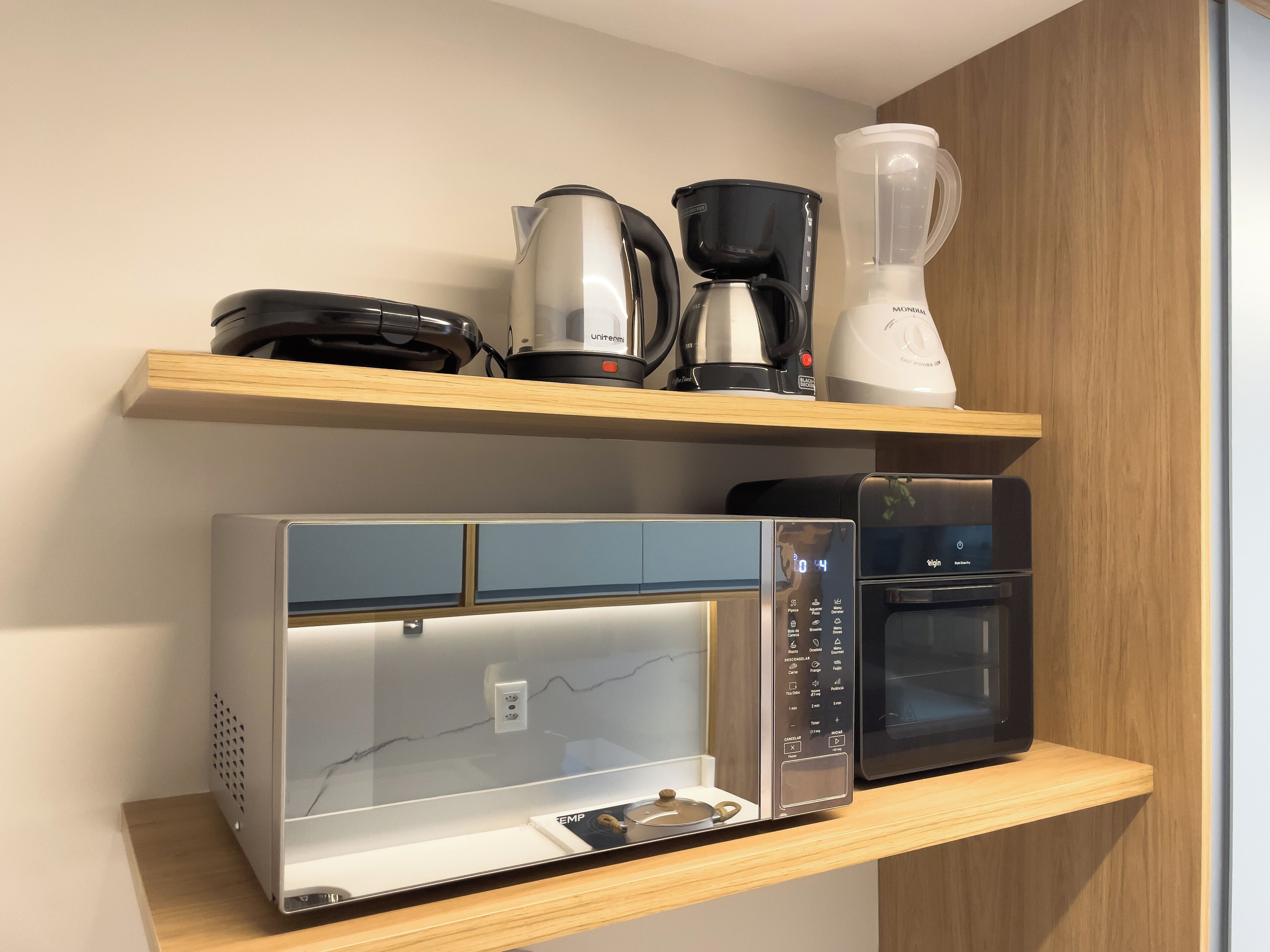 Eine Küche mit Kaffeemaschine, Mixer, Mikrowelle und digitaler Uhr.