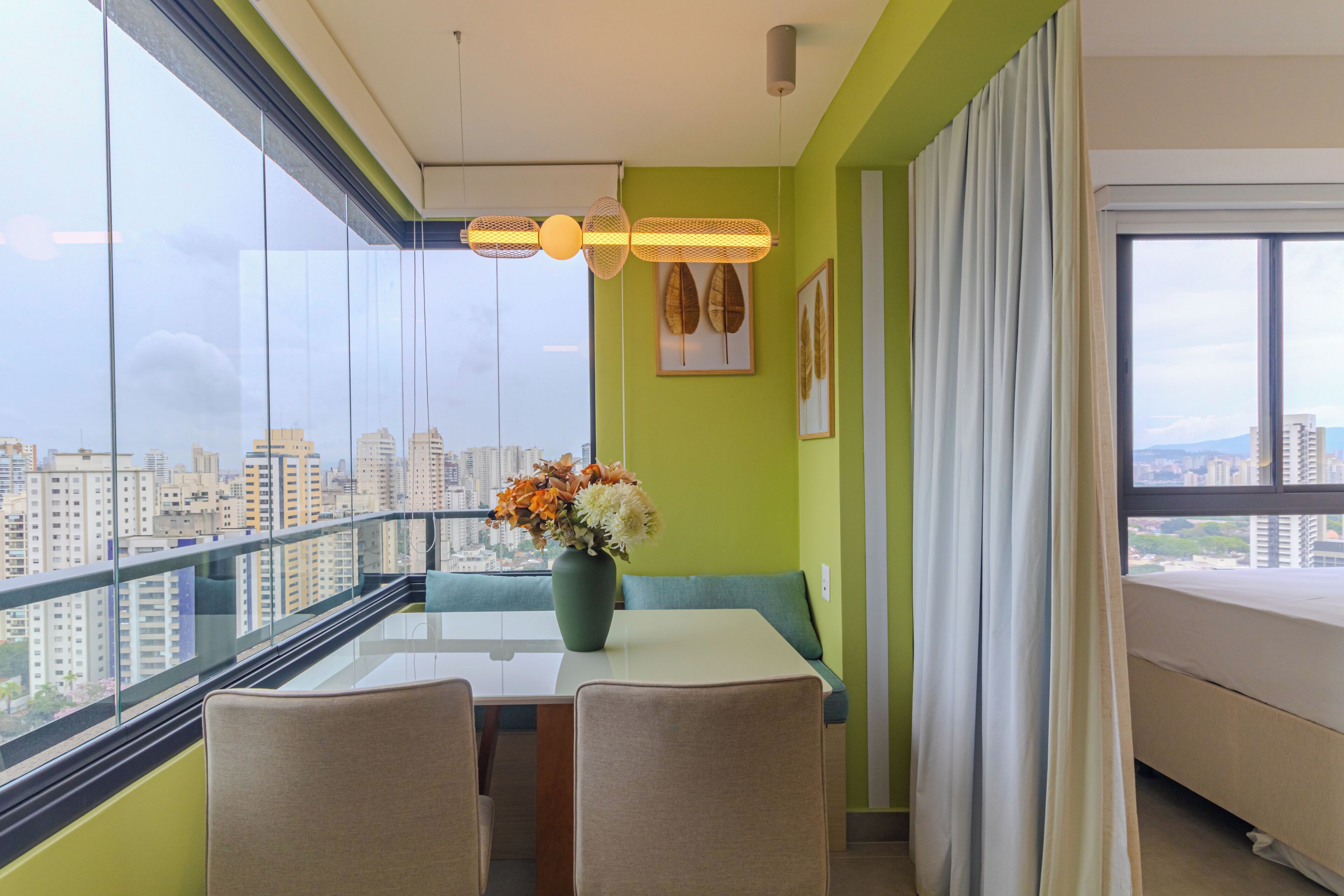 Un balcon avec une balustrade en verre, une table avec des chaises, un vase de fleurs et une vue sur la ville.