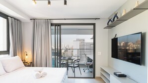 Ein modernes Hotelzimmer mit einem großen Bett, einem Flachbildfernseher, einem Balkon mit Blick auf die Stadt und einem Schreibtisch mit Stuhl.