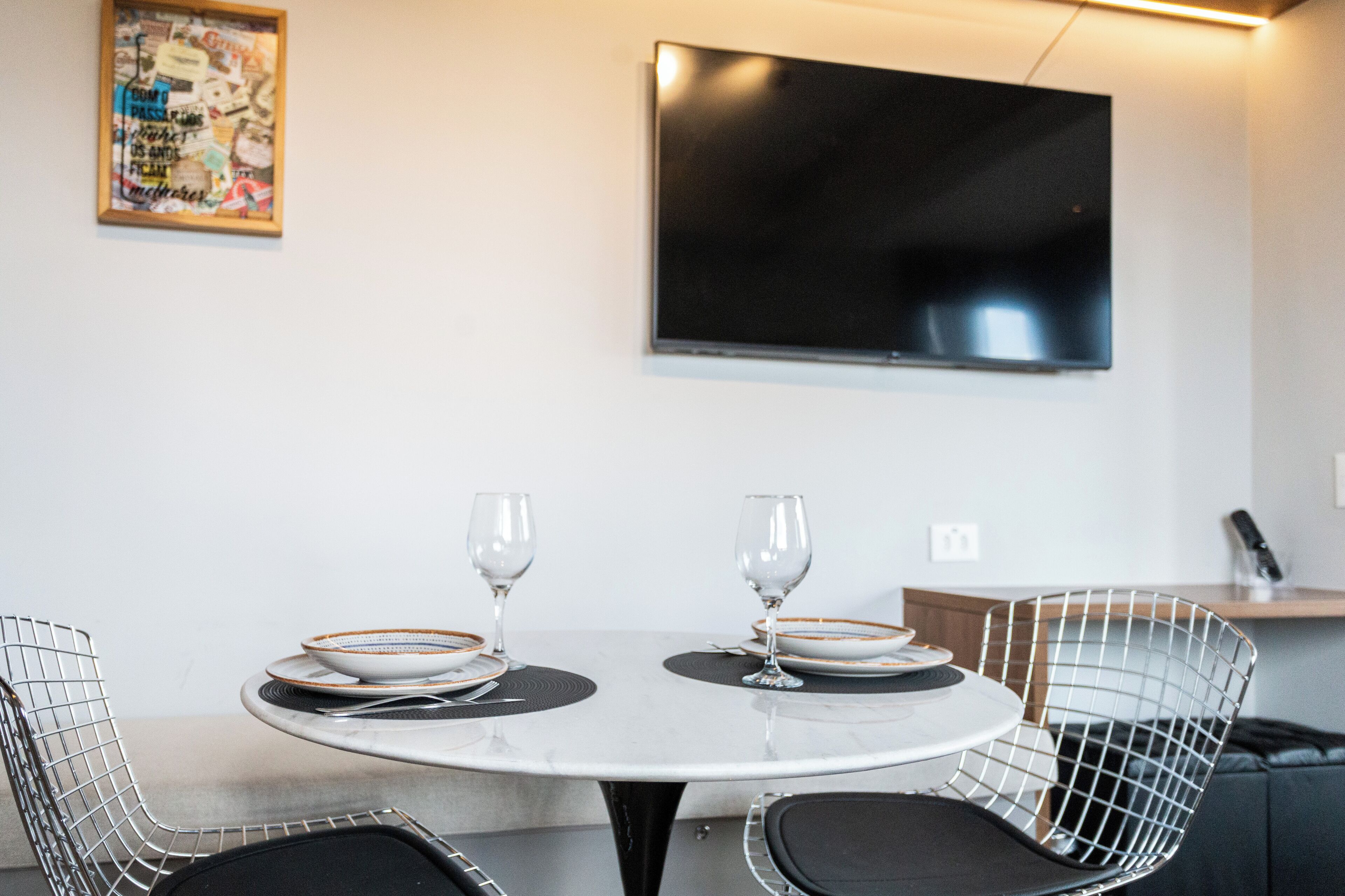 A dining area with a round table, two chairs, and a television mounted on the wall.
