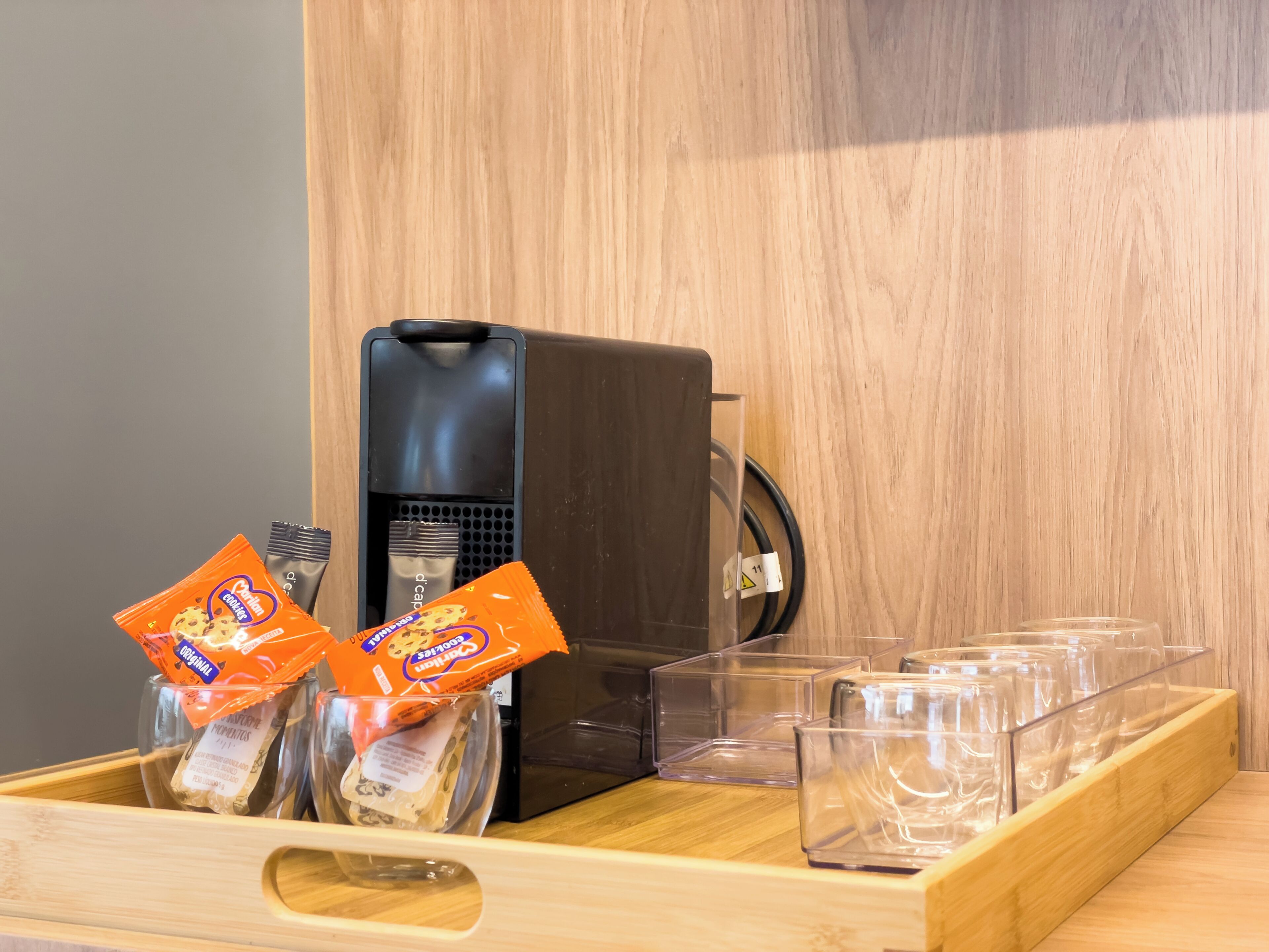 A coffee machine, two packets of cookies, and several clear glasses on a wooden tray.