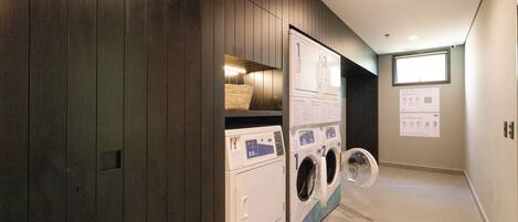 A laundry room with two washers and dryers, wooden paneling, a window, and a wall-mounted instruction sign.