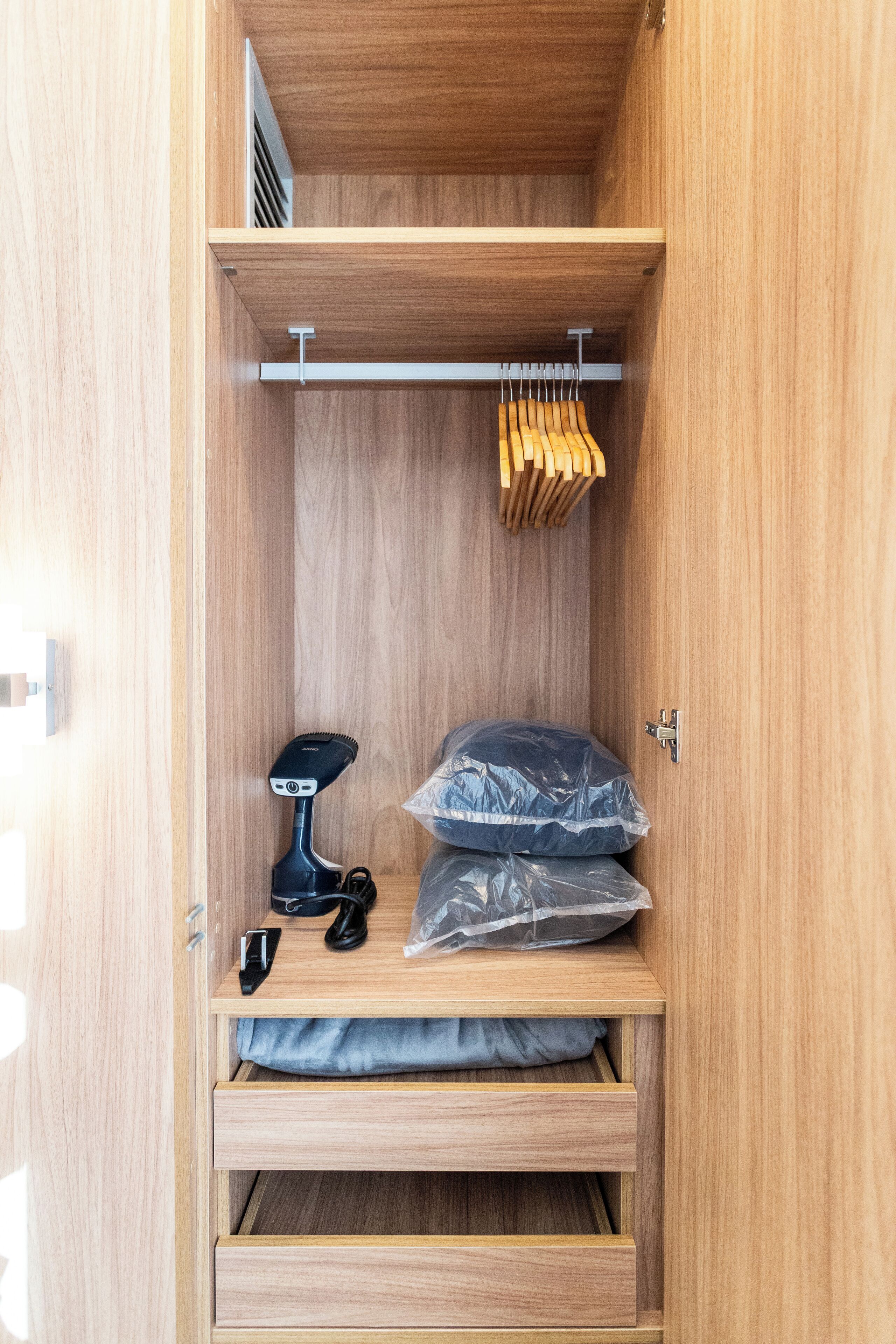 A wooden wardrobe with a hanging rack, a vacuum cleaner, and plastic bags.