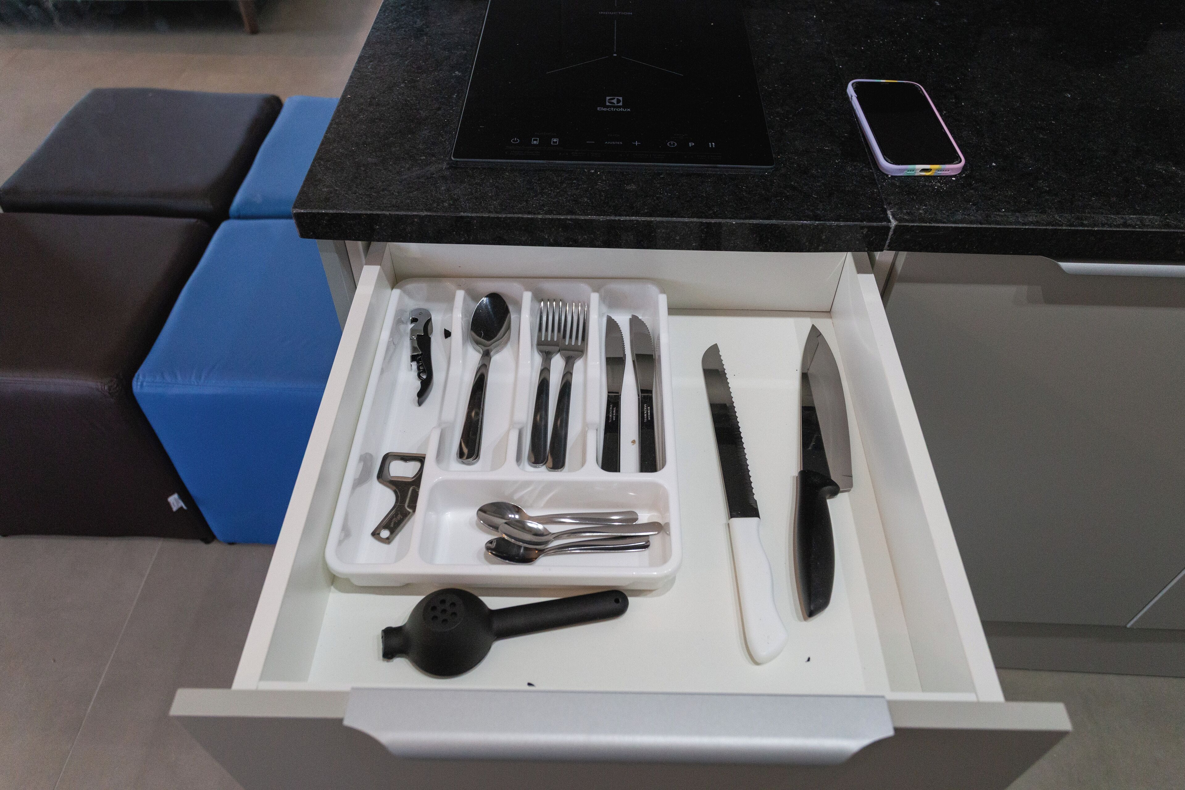 Un cajón de cocina con utensilios y un teléfono inteligente sobre la encimera.