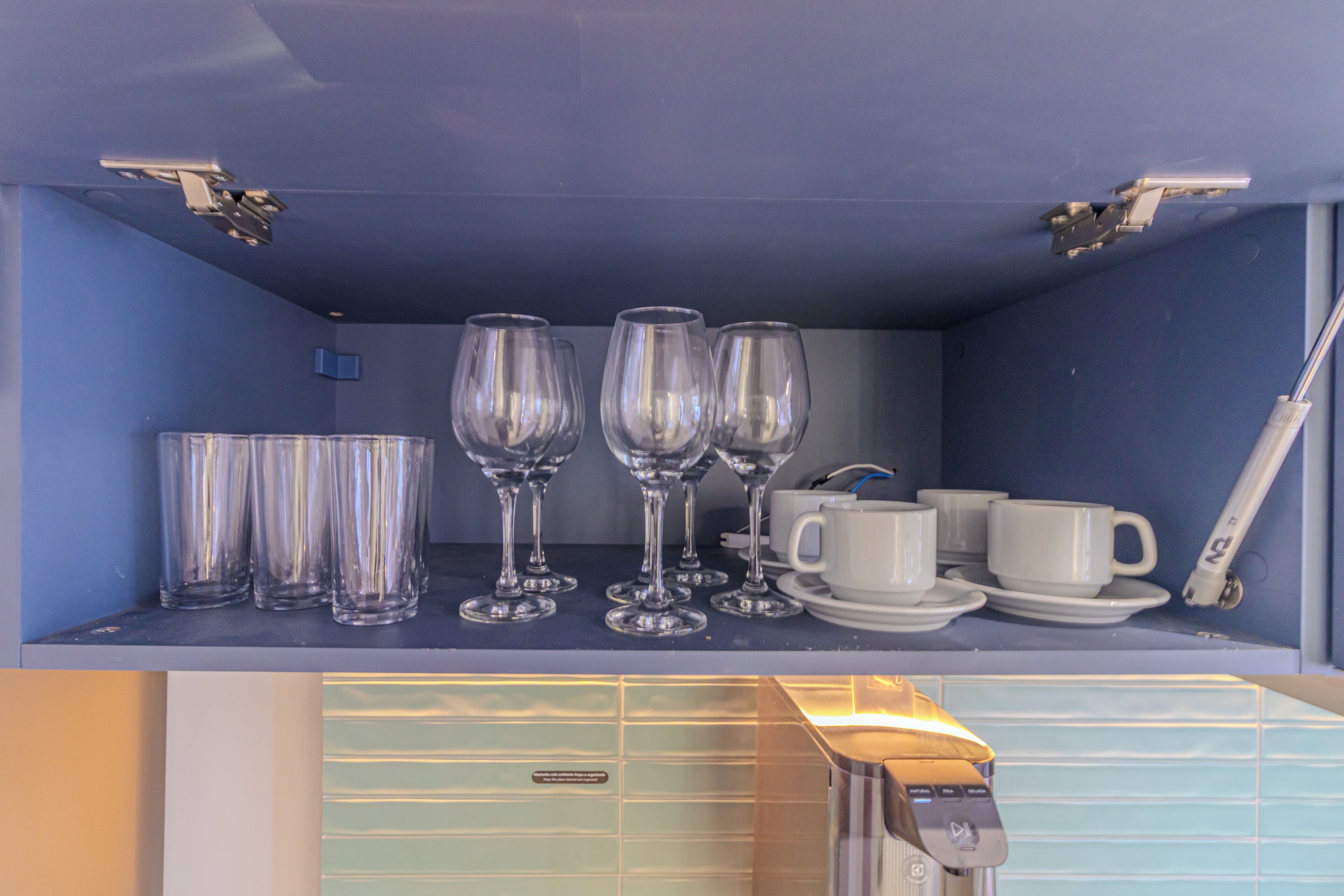 A shelf with wine glasses, cups, and a coffee maker.