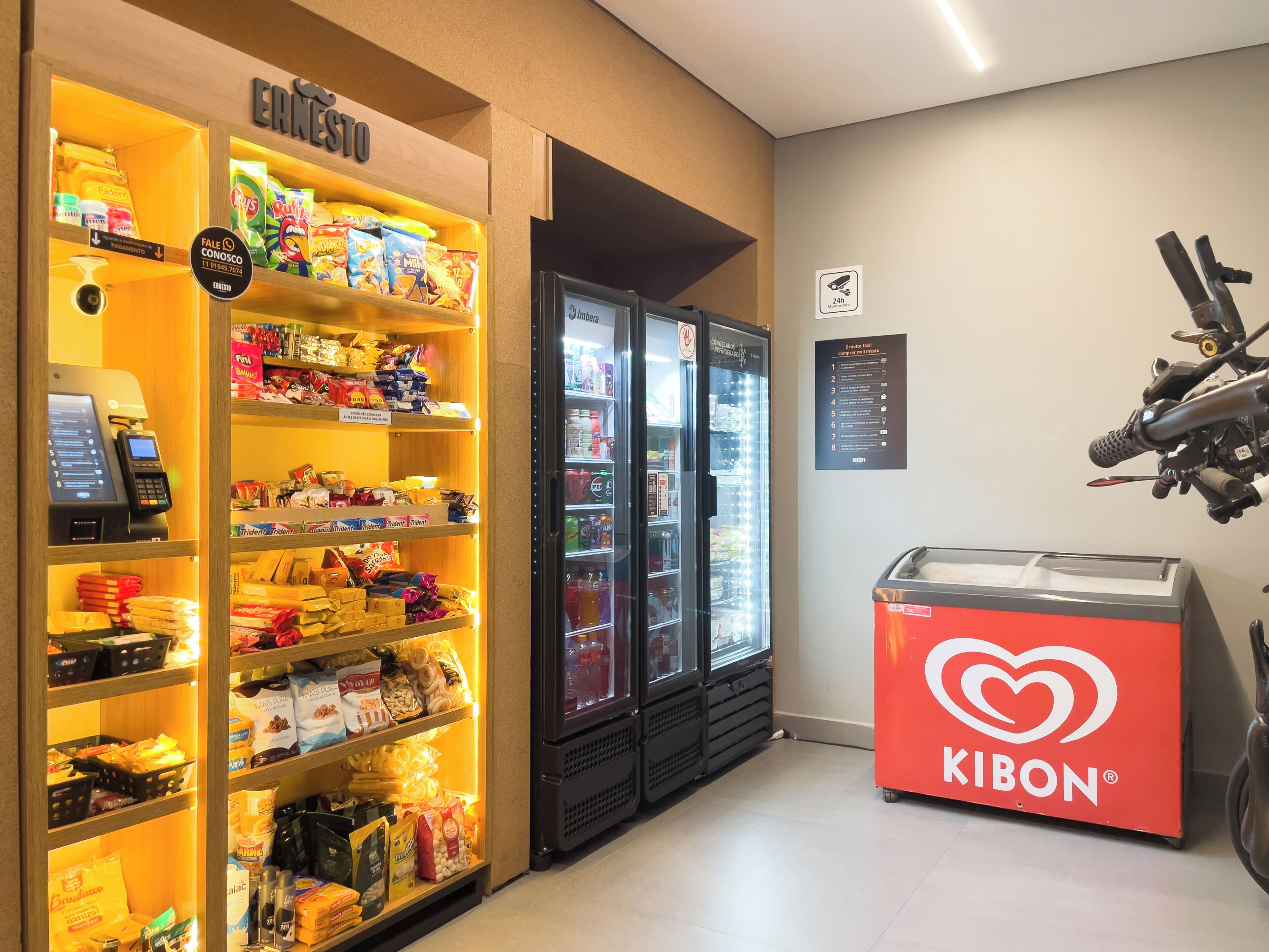 A snack and beverage kiosk with a variety of snacks and drinks, a Kibon ice cream display, and a vending machine.