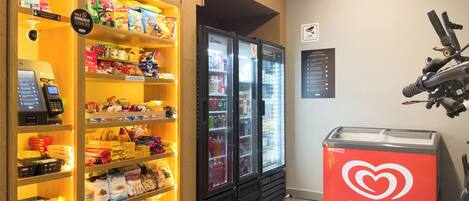 A snack and beverage kiosk with a variety of snacks and drinks, a Kibon ice cream display, and a vending machine.