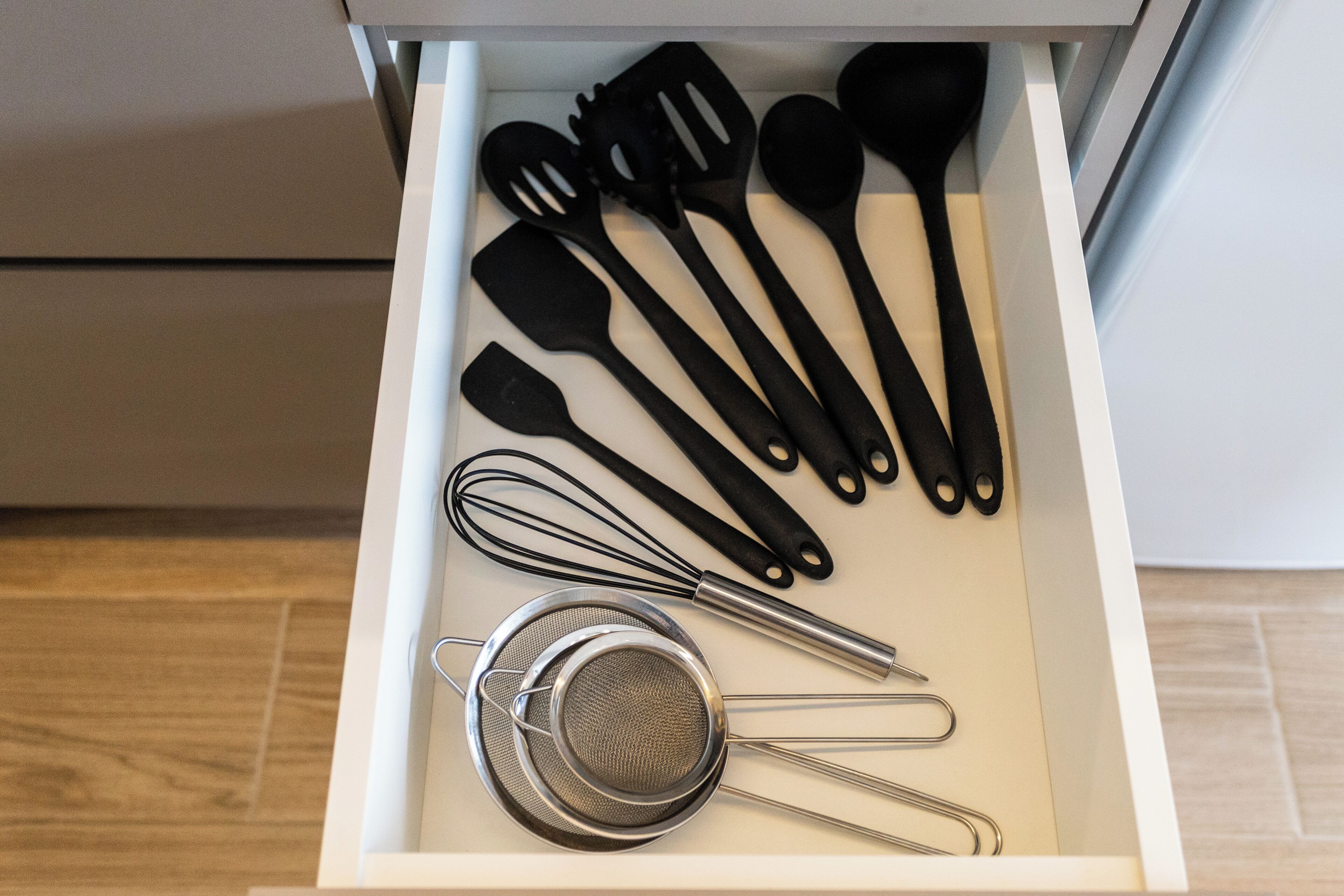 A drawer containing various kitchen utensils including spatulas, a whisk, and a strainer.