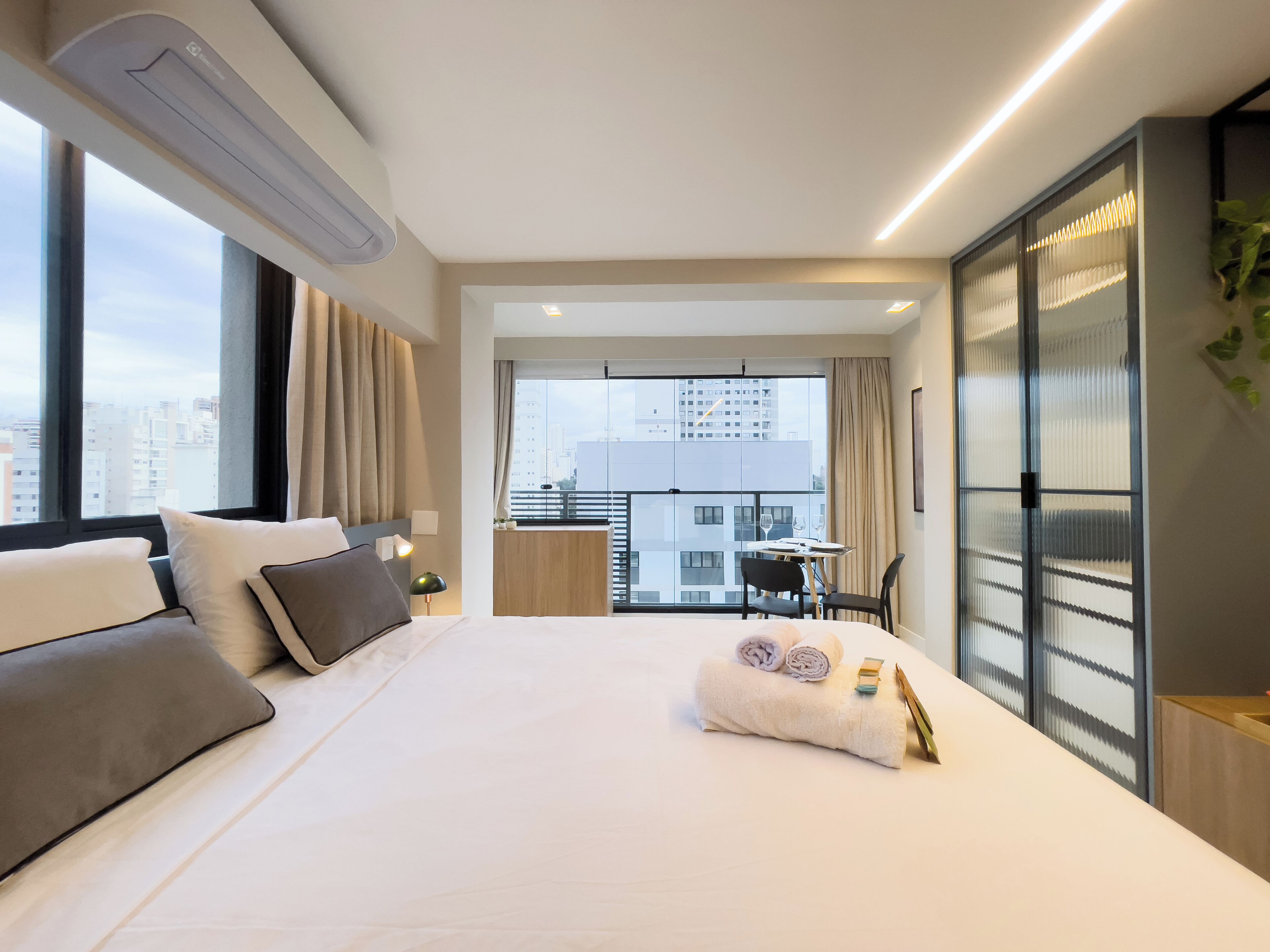 A modern hotel room with a large bed, a desk, and a view of the cityscape.