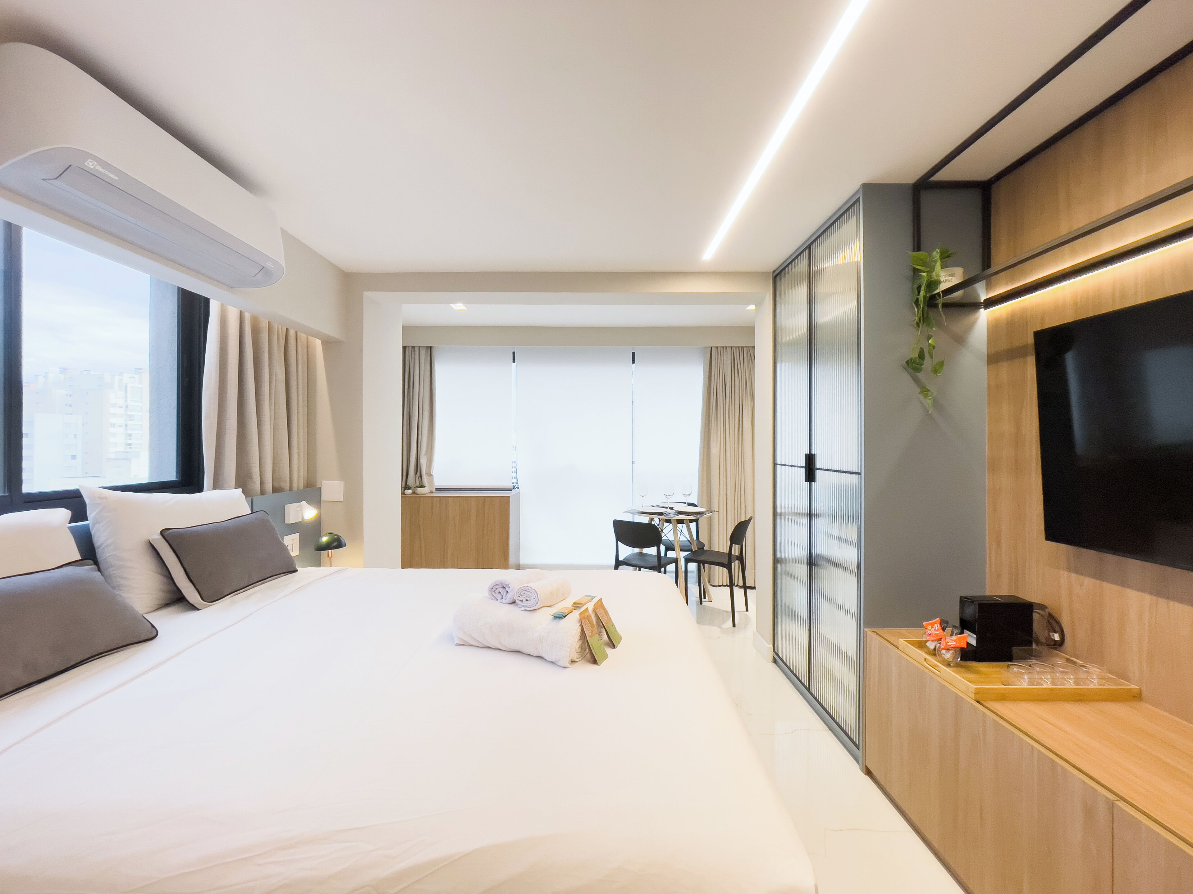 A modern hotel room with a large bed, a desk, a flat-screen TV, and a city view.