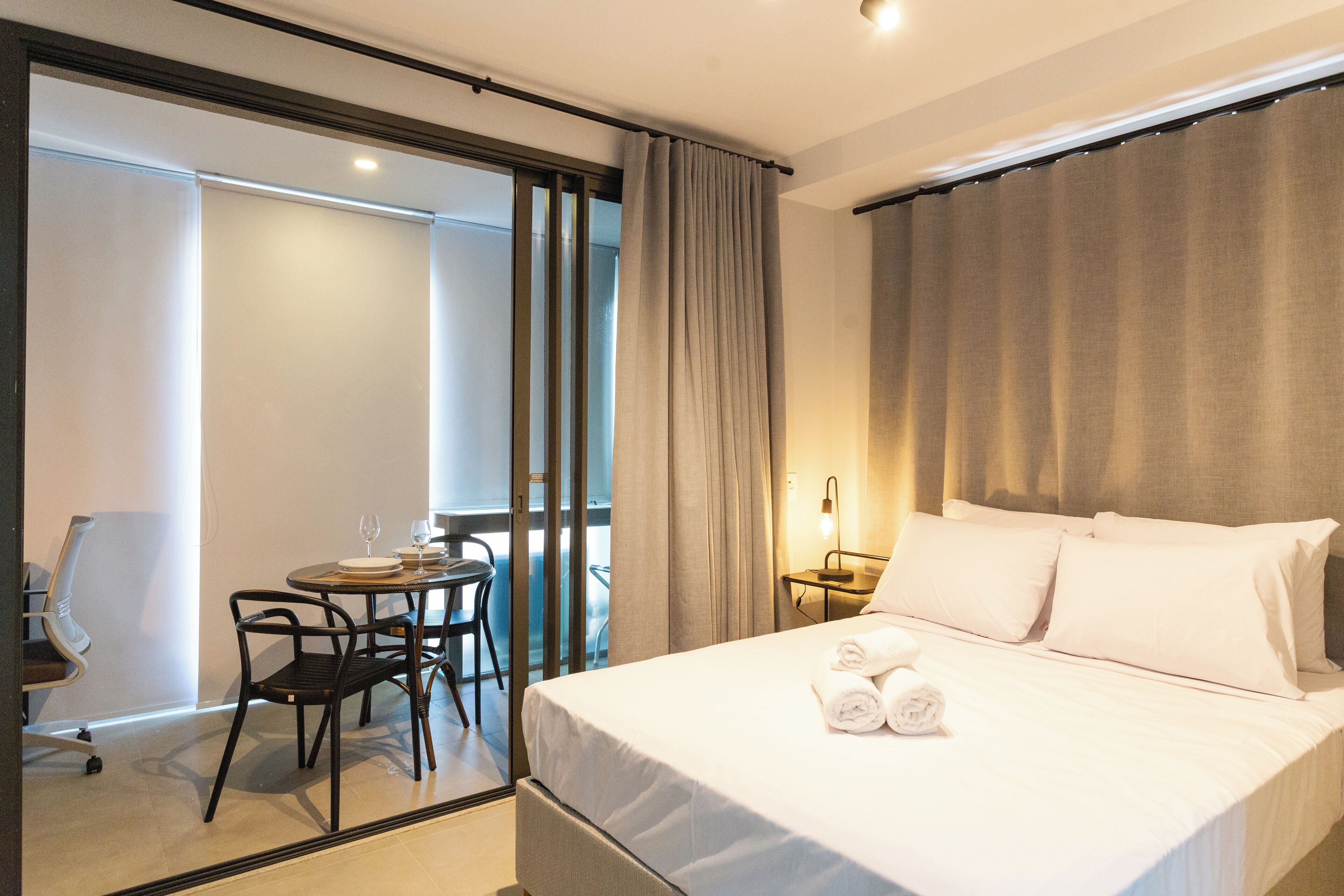 A hotel room with a bed, a desk with a chair, and a view through a sliding door.