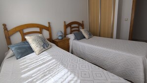 Una habitación con dos camas individuales, cabeceros de madera, una mesita de noche con lámpara y un armario con puertas correderas.