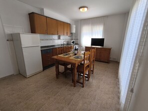 Una cocina compacta con armarios de madera, un refrigerador blanco y una mesa de comedor para dos.
