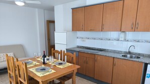 Un comedor con mesa de madera dispuesta para cuatro, una cocina con armarios de madera y encimera de granito, y un refrigerador blanco.