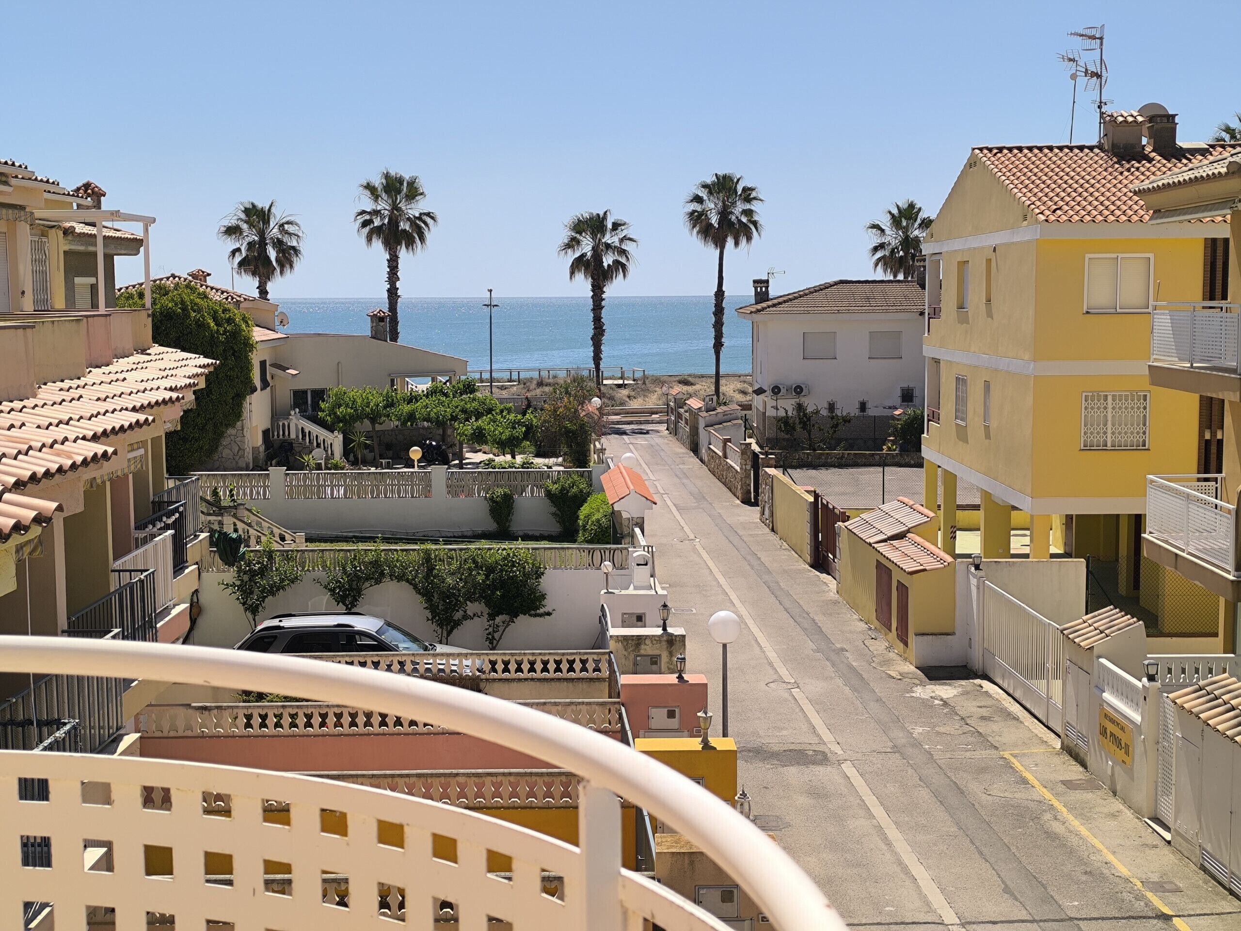 Eine Küstenstraße mit Gebäuden, Palmen und freiem Blick auf das Meer.