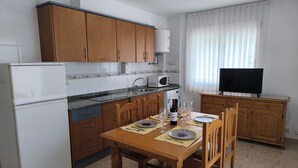 Cocina compacta con armarios de madera, microondas integrado y zona de comedor para cuatro.