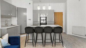 A modern kitchen with a central island, bar stools, a blue sofa, and a white radiator.