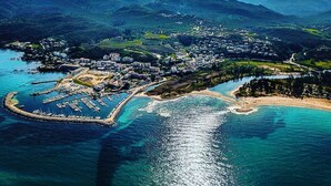 An aerial view of a coastal town with a marina, buildings, and surrounding mountains.
