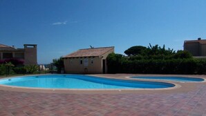 A swimming pool with a tiled deck, surrounded by buildings and greenery.