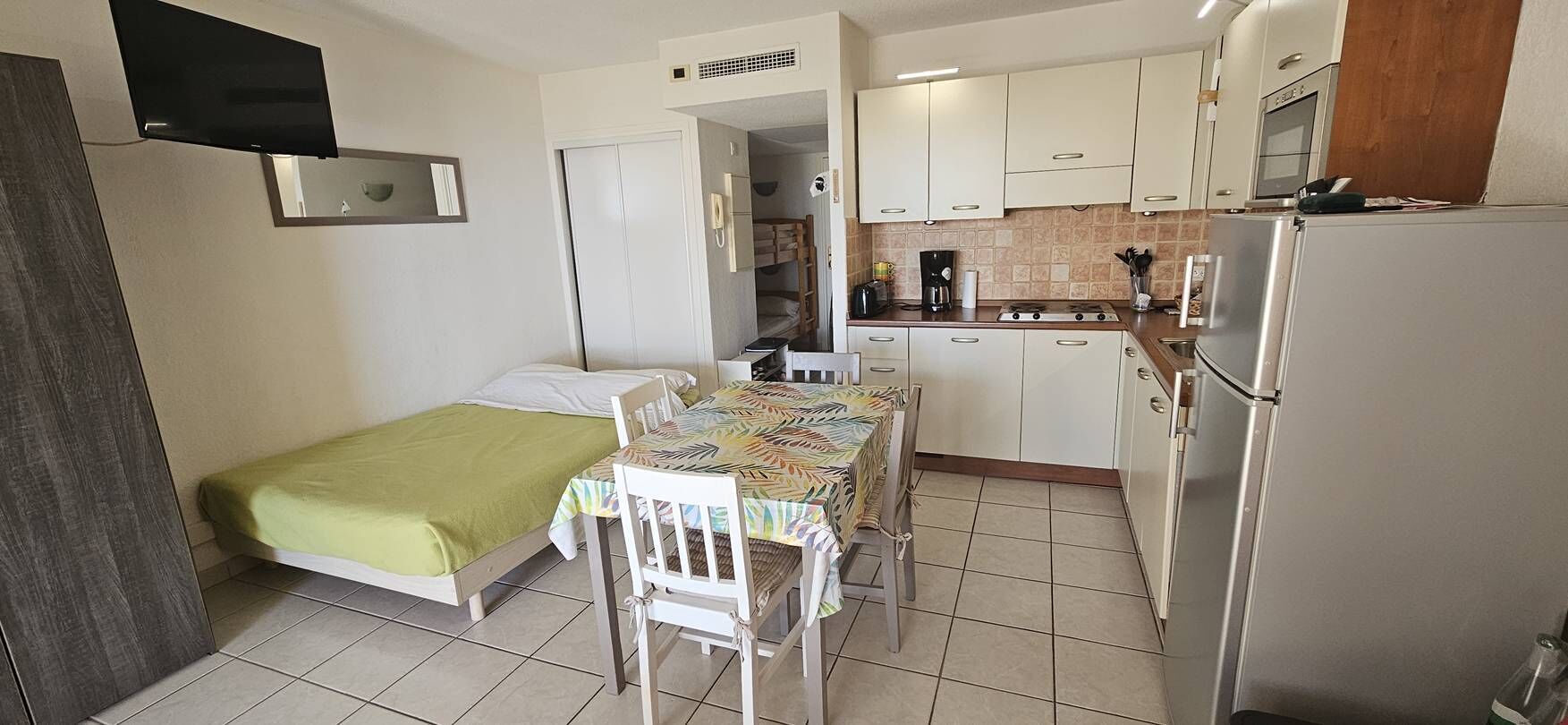 A compact room with a bed, a small dining table, and a kitchenette.