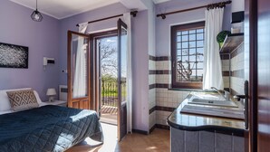 Un dormitorio con cama, mesita de noche, cortinas y vistas al exterior.
