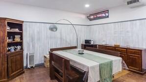 Una habitación compacta con una mesa de comedor de madera, una silla, un armario con libros, un radiador, un microondas y un televisor montado en la pared.