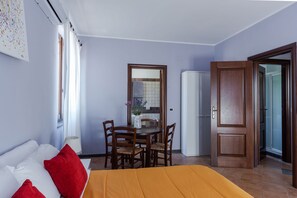 A hotel room with a bed, a dining table with chairs, a refrigerator, and a wooden door. - Il Baglio Dell Etna by Wonderful Italy (Linguaglossa)