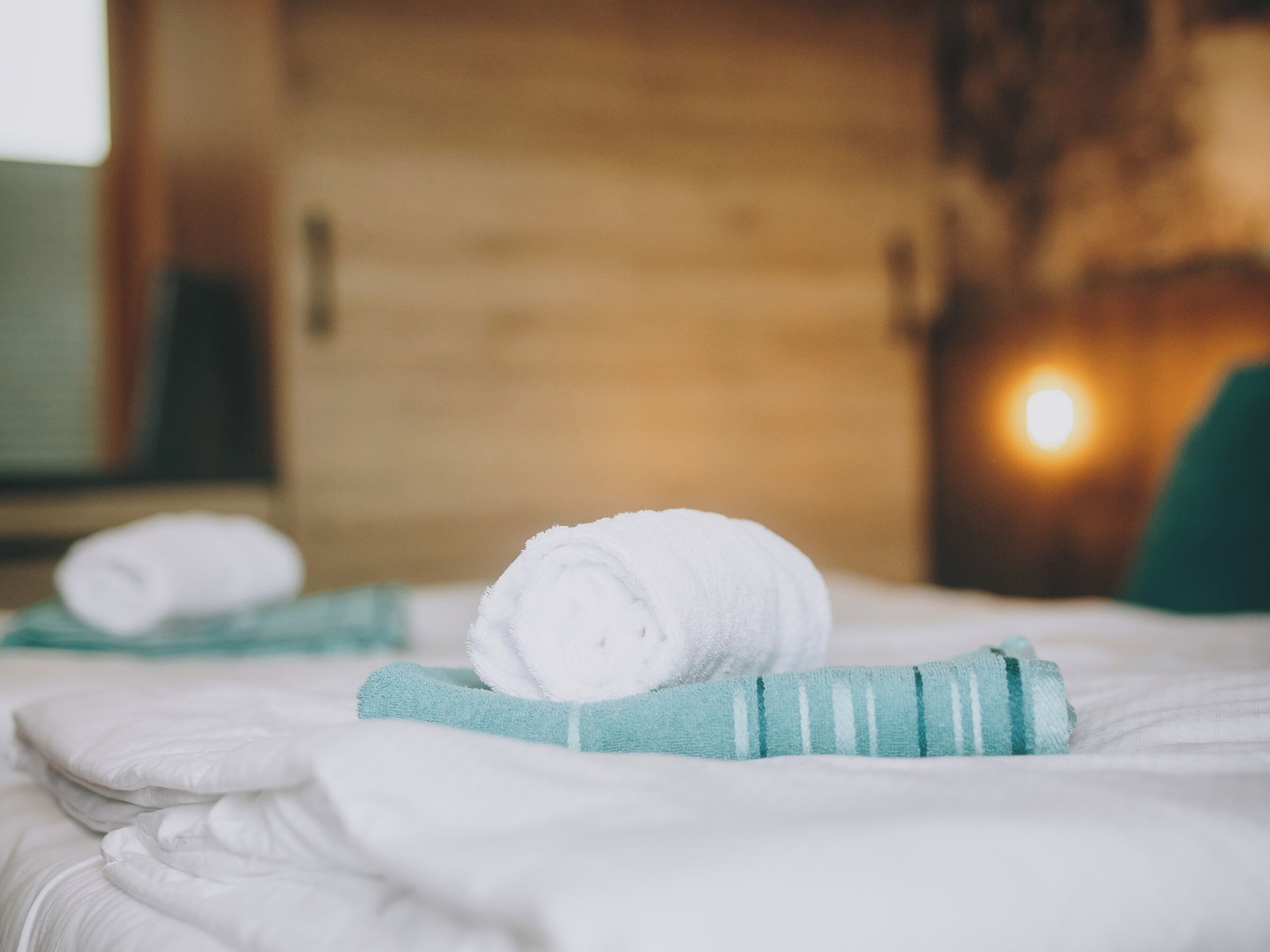 A neatly made bed with white linens and a rolled white towel on top.