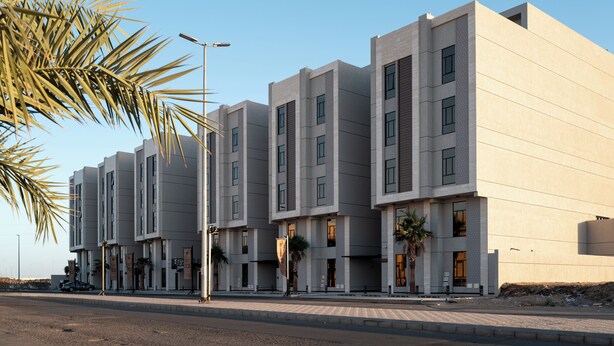 Un bâtiment moderne à la façade symétrique, doté de nombreuses fenêtres et bordé de palmiers.