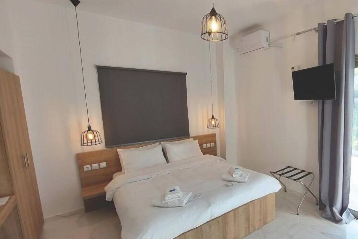 Une chambre moderne avec un lit en bois, deux tables de chevet, une grande fenêtre avec des rideaux, un téléviseur à écran plat fixé au mur et un luminaire au plafond.