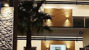 Un edificio moderno con una piscina reflectante, una palmera y un muro de madera.