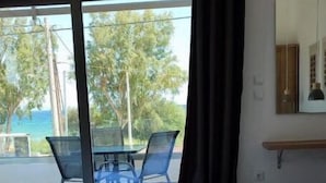 Habitación de hotel con una cama, una mesa con sillas, vista al océano y cortinas en la ventana.