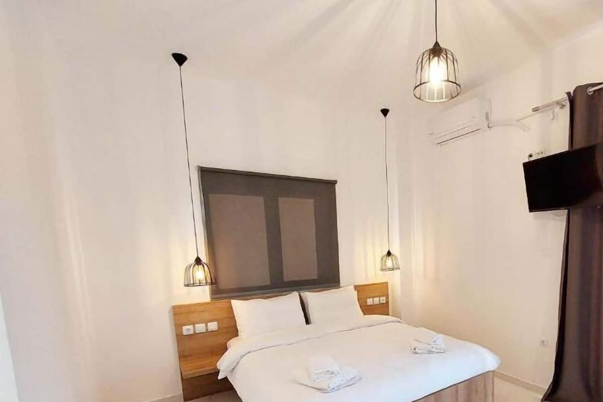 Une chambre d’hôtel avec un lit, deux tables de chevet, une fenêtre et deux lampes suspendues.
