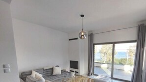 Una sala moderna con sofá, una mesa de centro de vidrio, un televisor de pantalla plana y un amplio ventanal con cortinas.