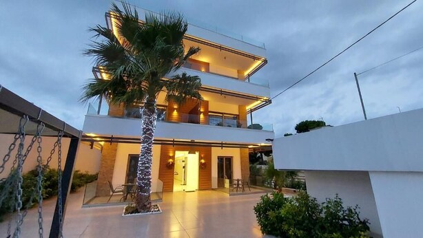 Una casa moderna de dos pisos con un balcón, una palmera y una entrada bien iluminada.