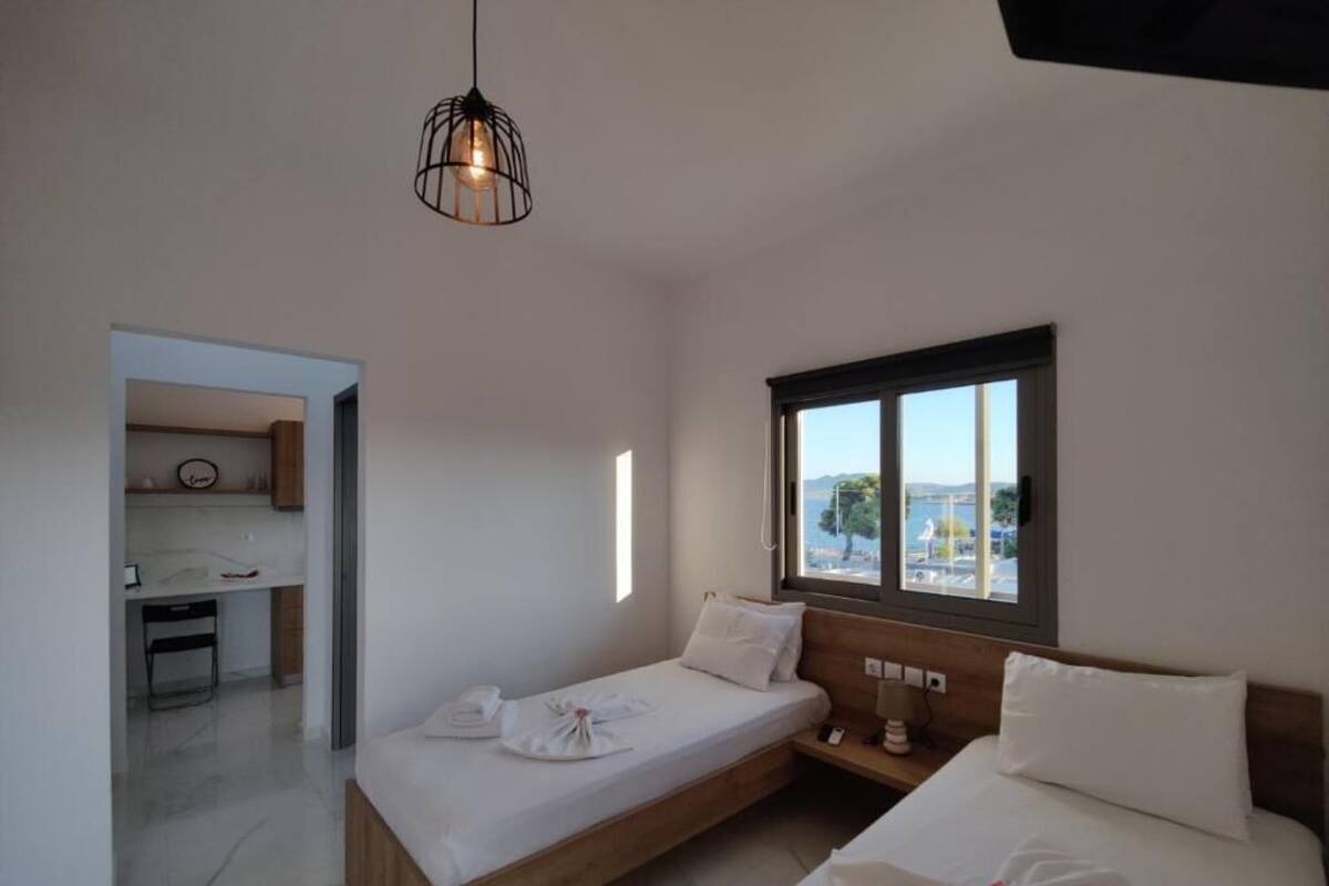Une chambre d’hôtel moderne avec deux lits, une kitchenette et une grande fenêtre donnant sur l’extérieur.