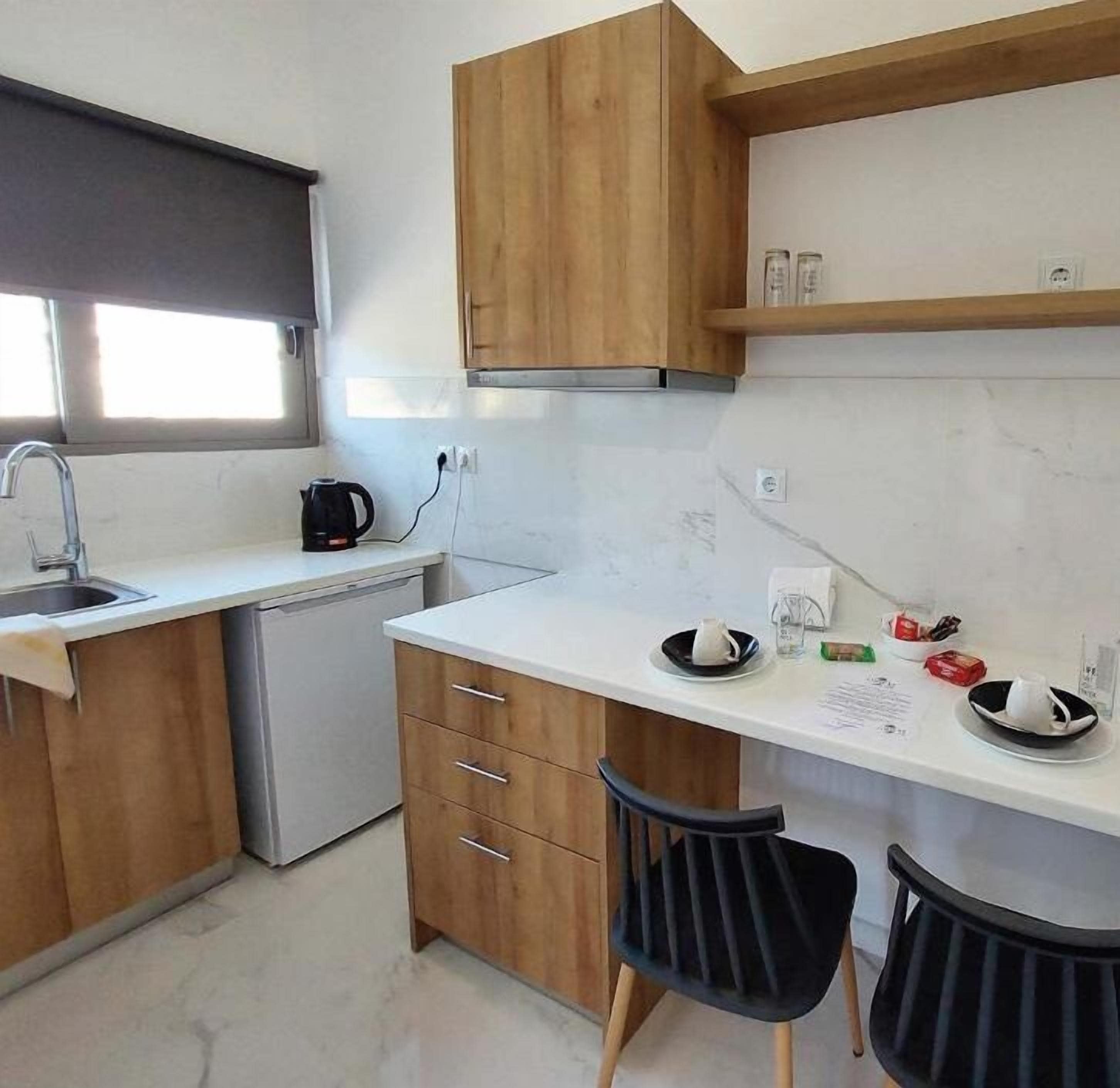 Una cocina compacta con armarios de madera, encimera blanca, un lavabo, cafetera y dos sillas negras.