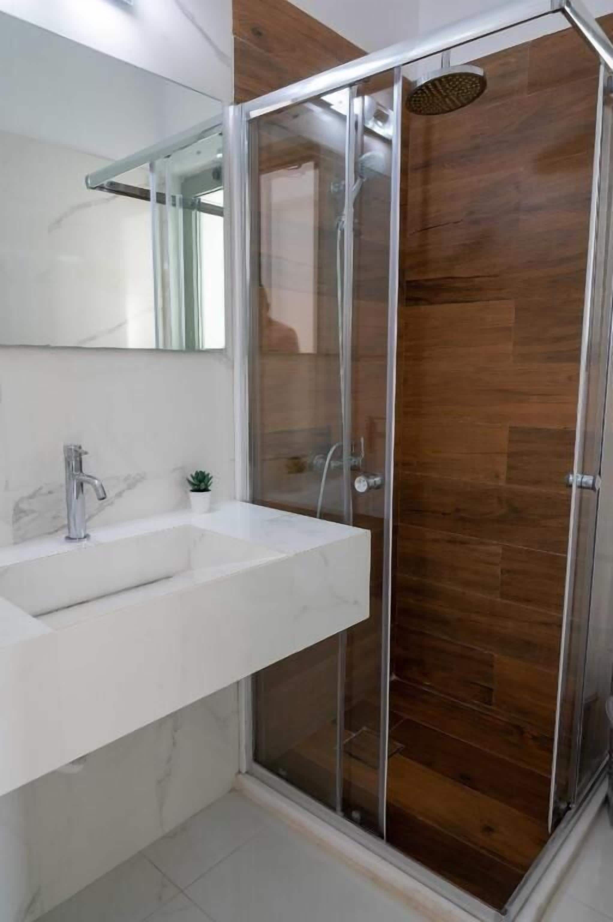 Un baño moderno con ducha de vidrio, lavamanos de mármol y pared de madera.