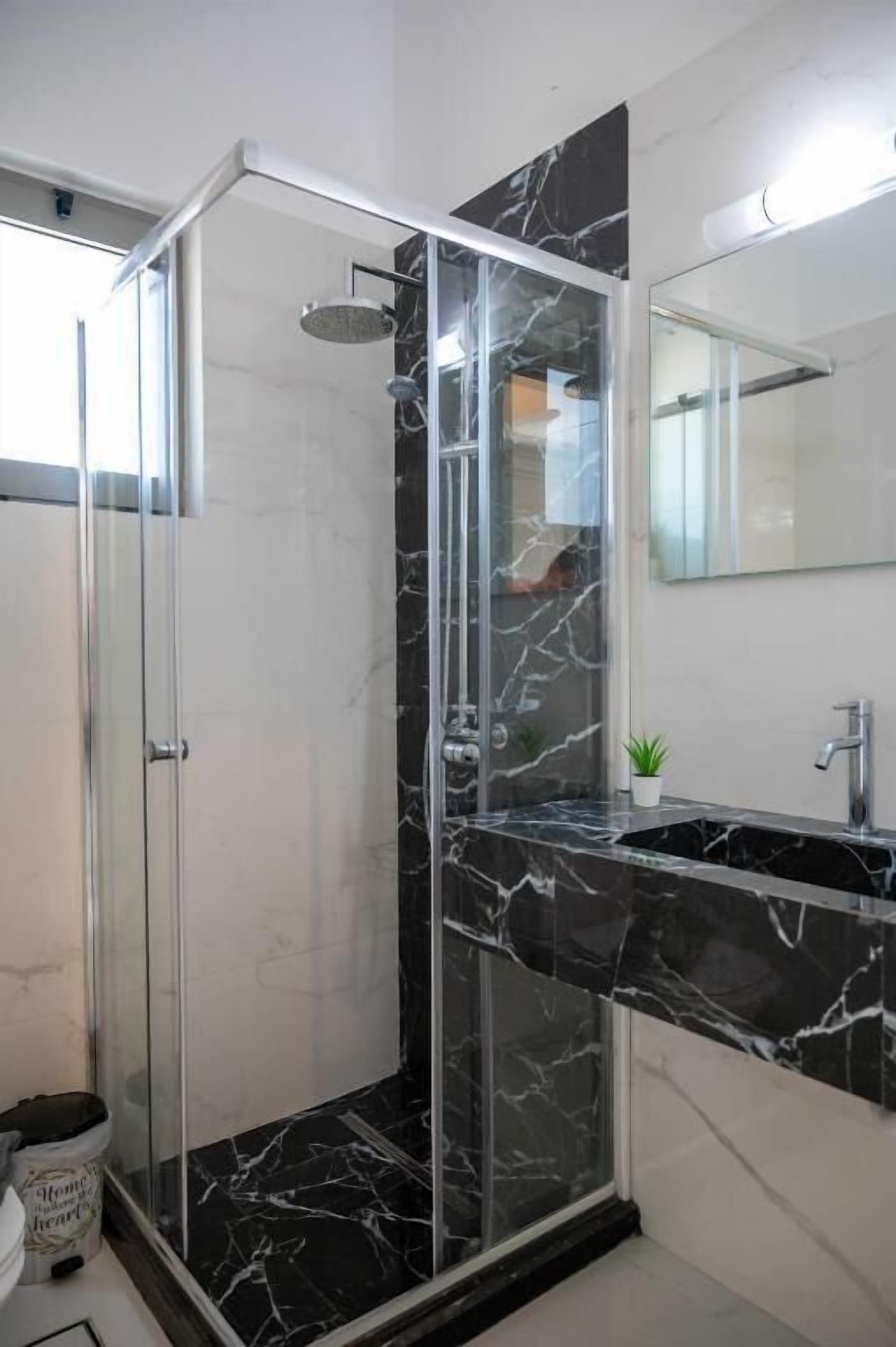 A modern bathroom with a glass-enclosed shower, a marble sink, and a small potted plant.