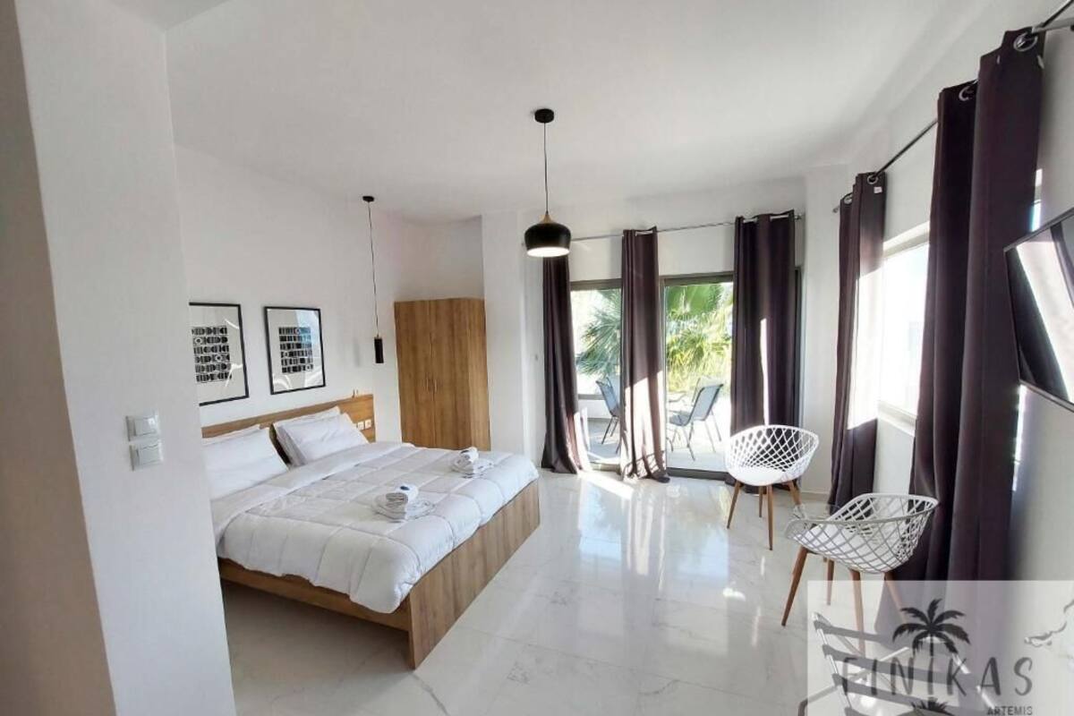 Une chambre moderne avec un lit, une tête de lit en bois, une chaise blanche et un balcon avec des rideaux.