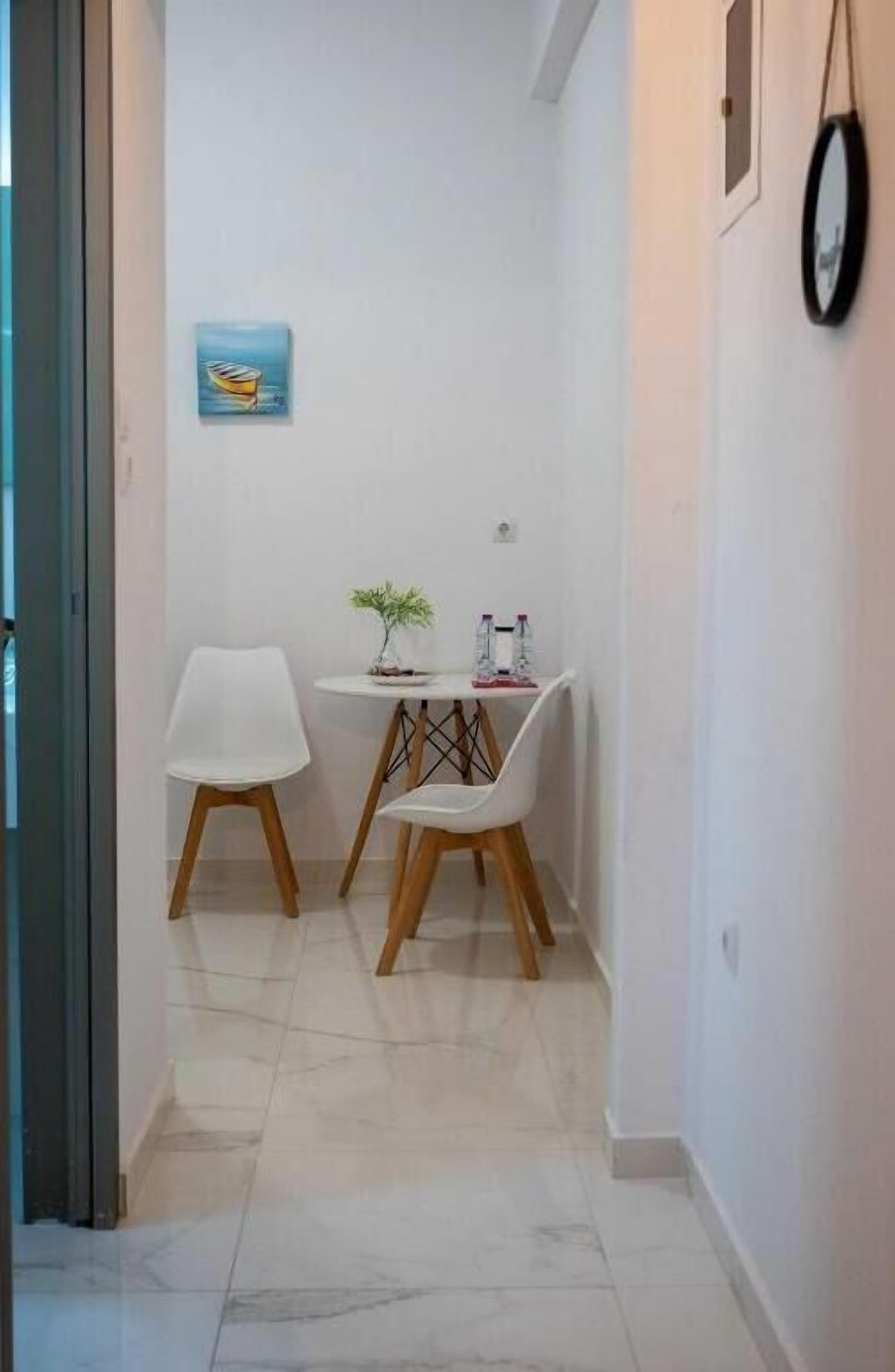 Un couloir étroit avec une petite table et deux chaises, une plante en pot et un tableau encadré au mur.