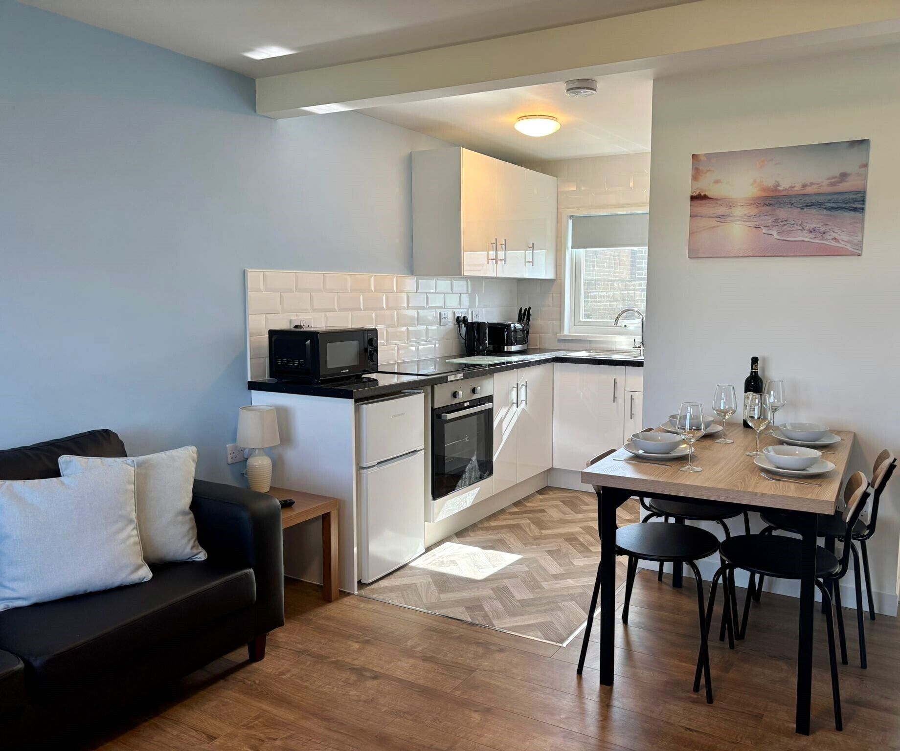 A compact kitchen with white cabinets, a microwave, and a stove. There is a dining table with chairs and a painting on the wall.
