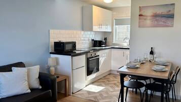 A compact kitchen with white cabinets, a microwave, and a stove. There is a dining table with chairs and a painting on the wall.